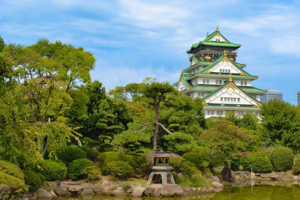Osaka Castle with green roofs above a traditional garden and stone lantern, a Tokyo or Osaka travel guide