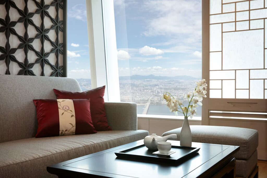 Signiel Seoul Hotel: A High-Altitude Stay Above the City Sofa with red pillows and tea set by a window viewing the Seoul skyline and river.