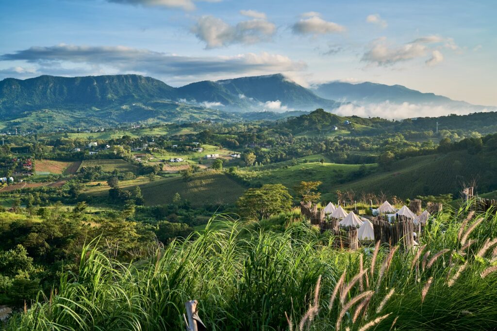 Green valley of hills, farmland and misty mountains under a blue sky in northern Thailand.