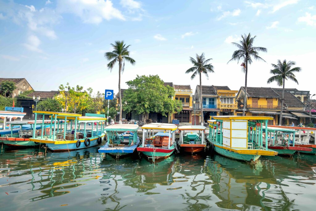 Vietnam Travel Budget: When Cheap Doesn’t Mean Simple Colorful wooden boats on the river by Hoi An old town houses, a Vietnam travel budget guide