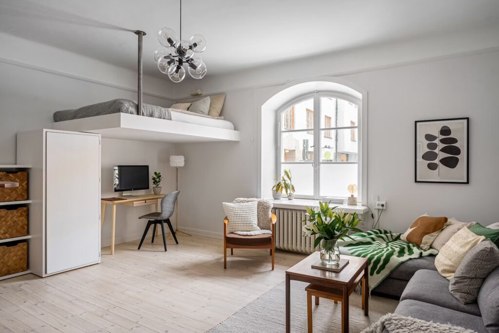 What Living Cheap Actually Costs Over Time Compact Scandinavian studio apartment with a loft bed above a workspace and small living area