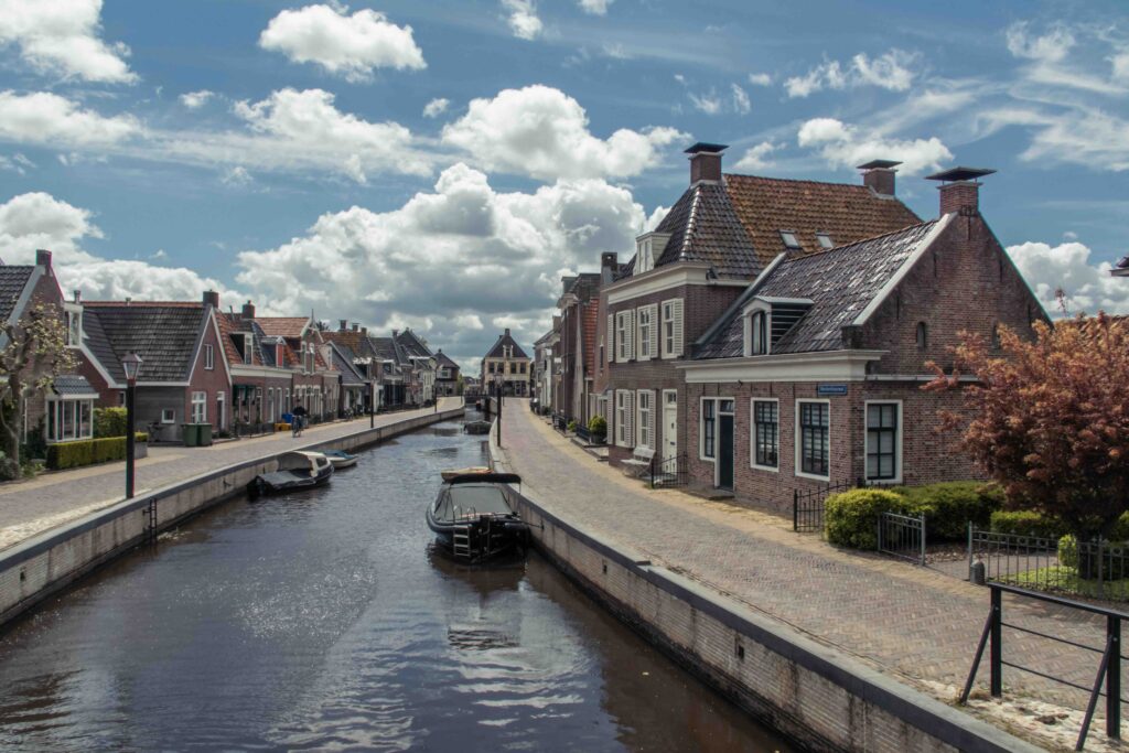 Quiet Dutch canal town with brick houses, moored boats and cobbled streets under a bright sky