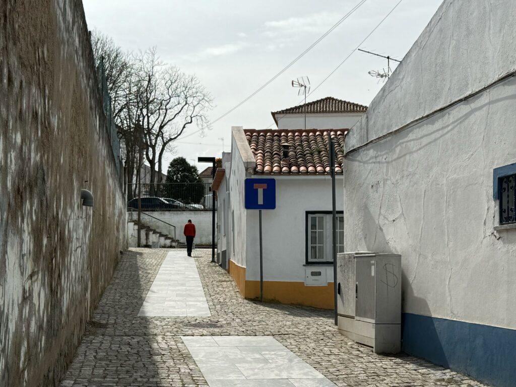 A lone man in a red jacket walking into a narrow dead-end alley in a quiet Portuguese town