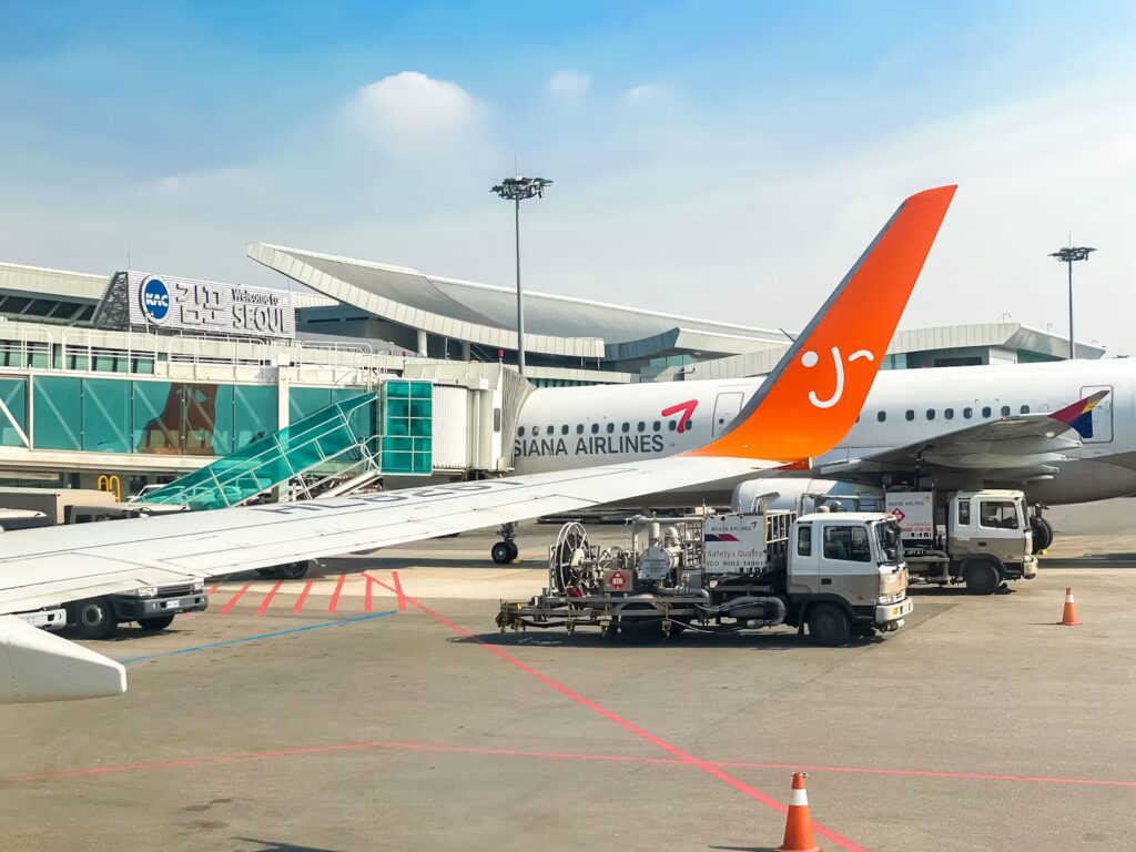 The bright orange tail of an Asiana Airlines airplane parked at an airport gate on a sunny day.