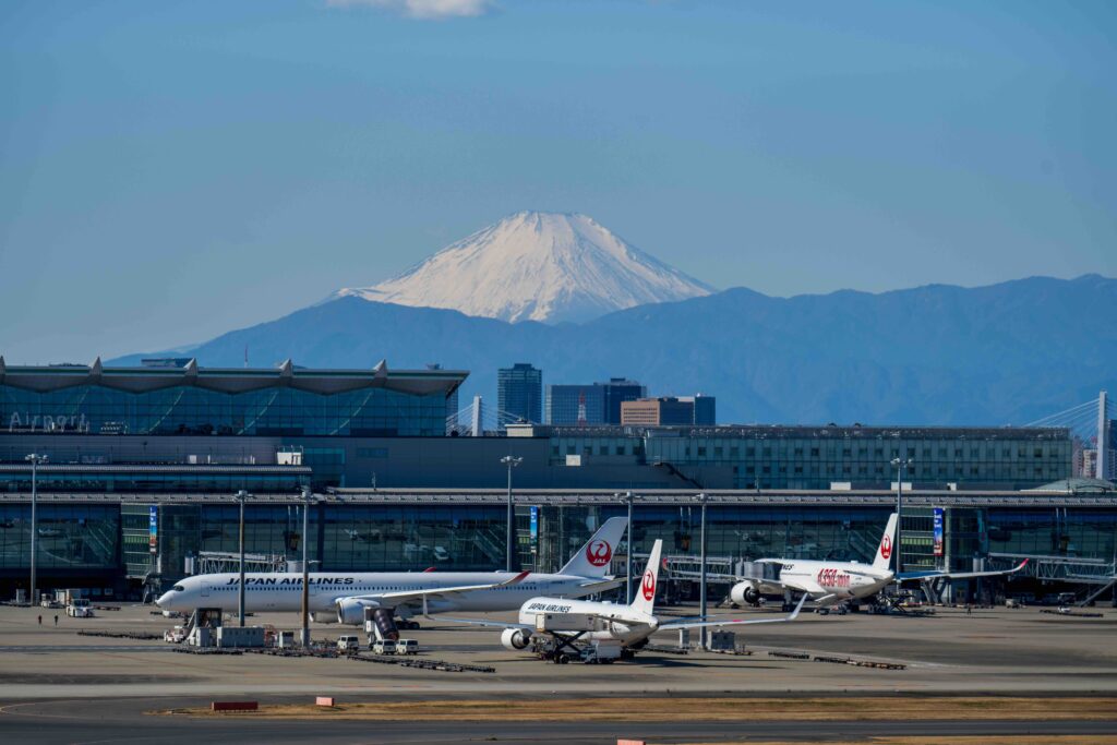 Passenger airplanes parked at a Tokyo airport terminal with snow-capped Mount Fuji in the background.