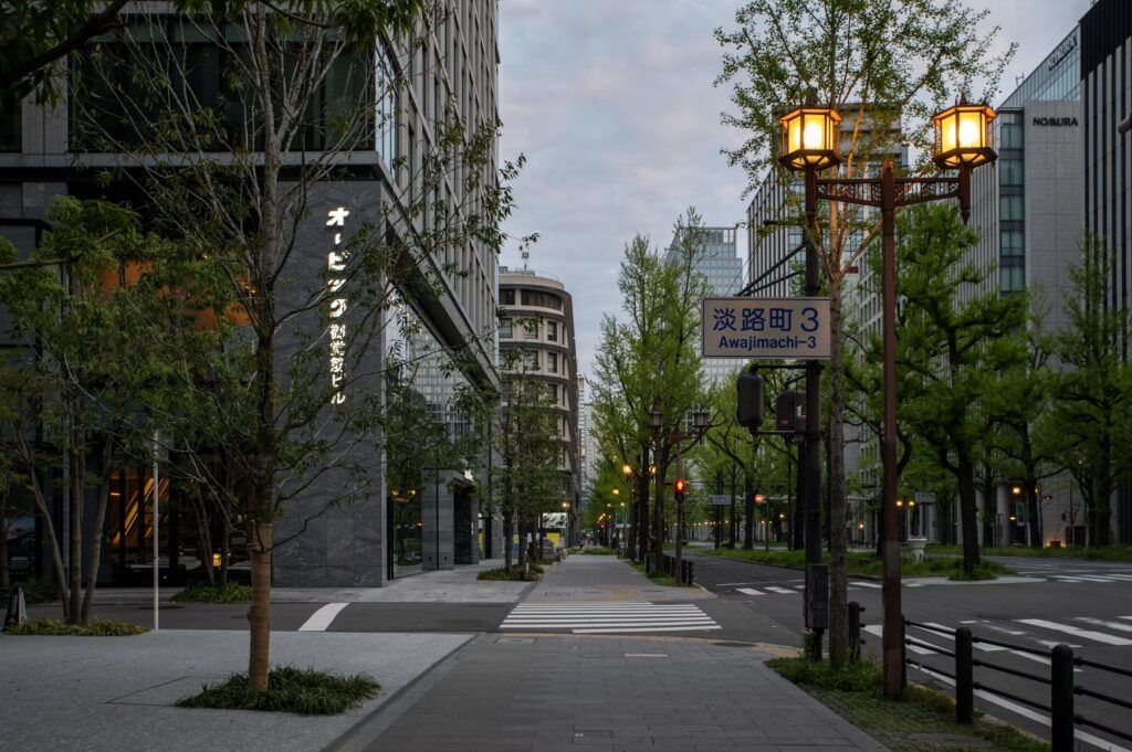 Quiet tree-lined Osaka street at dusk with glowing lanterns and empty sidewalks in Japan