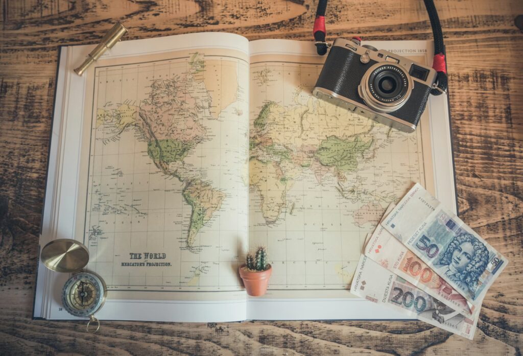 World map with banknotes, compass and camera laid out for trip planning, how to set a travel budget