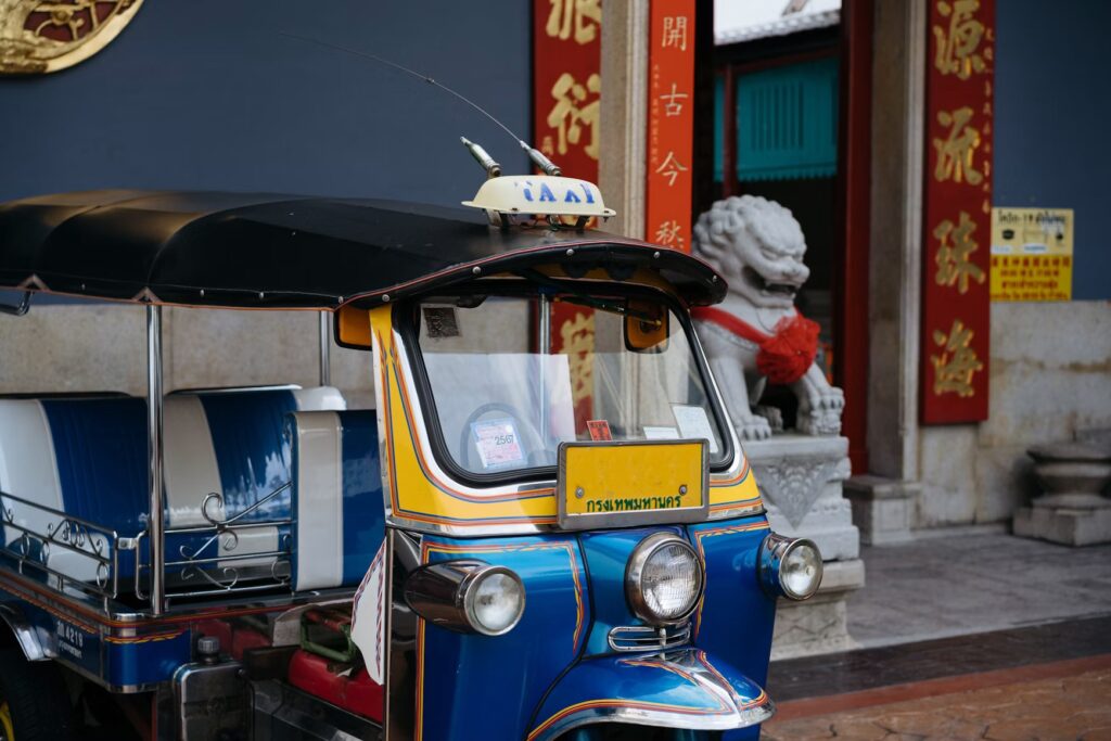 Colorful blue and yellow tuk-tuk parked by a Chinese shrine lion in Bangkok, Thailand.