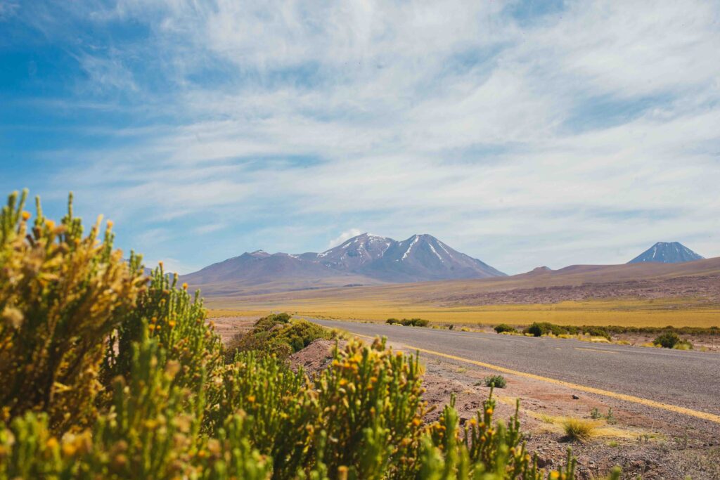 How to Plan a Road Trip Through Chile: The Ultimate Guide from Patagonia to the Atacama Desert Empty desert highway with yellow center line leading toward volcanic peaks in Chile's Atacama Desert