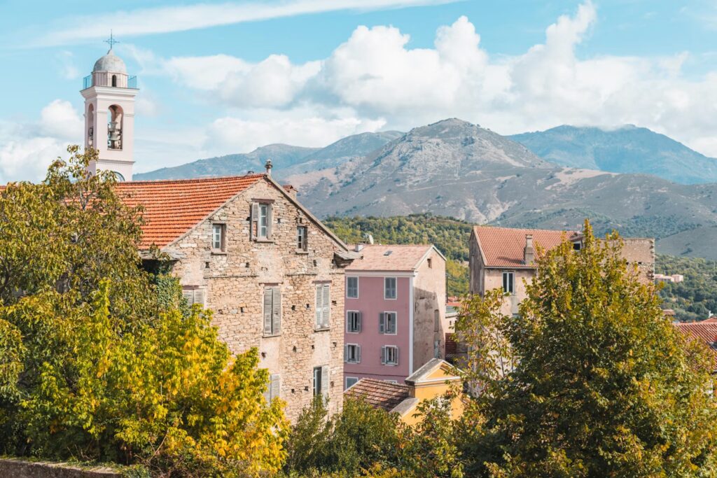 Corsica Travel Guide: Hidden Beaches, Mountain Adventures, and Must-See Spots on the Island Stone village with a bell tower below rugged mountains on the island of Corsica