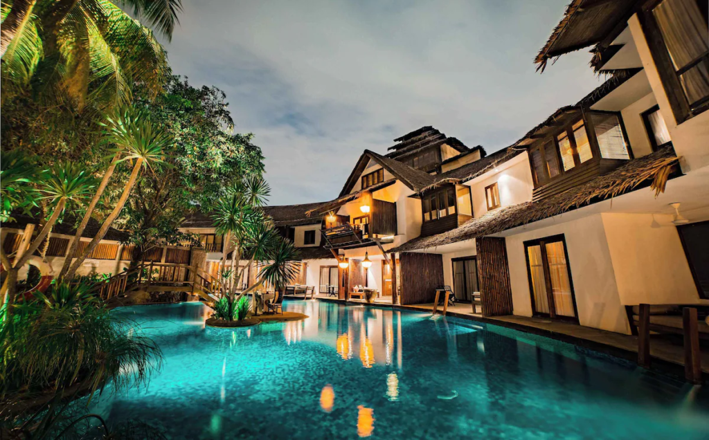 A stunning outdoor swimming pool at Villa Samadhi surrounded by tropical greenery and traditional wooden structures.