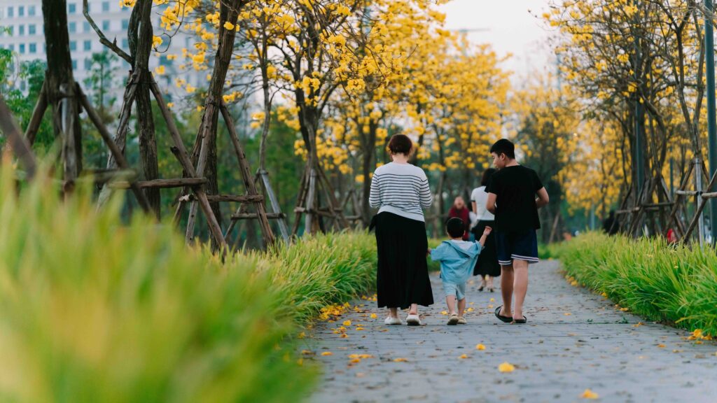 The Ultimate Guide to Planning a Family Vacation to Vietnam: Tips for Parents and Kids A family walking together along a paved park path lined with beautiful yellow blooming trees.