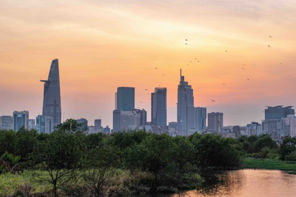 Flying from Hanoi to Ho Chi Minh City: A Quick Flight Connecting North and South Vietnam A beautiful, hazy sunset view of the Ho Chi Minh City skyline featuring the Bitexco Financial Tower and lush green trees.