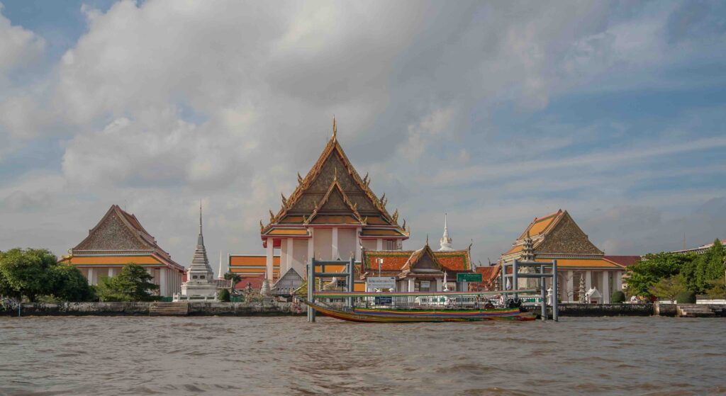 Flying from Hanoi to Bangkok: What the Flight Is Like to Thailand’s Bustling Capital Traditional Thai boats navigating the wide Chao Phraya River, passing several ornate Buddhist temples.