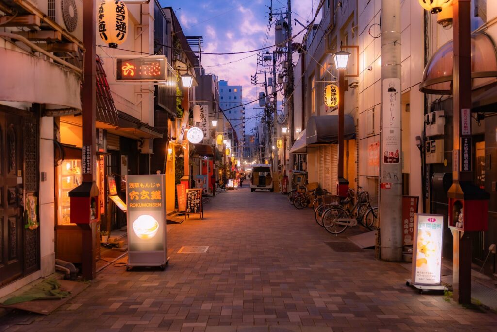 The Ultimate Guide to Planning a Foodie Trip in Japan: Must-Visit Restaurants and Local Markets A quiet Japanese street at twilight, lined with restaurants, glowing signs, and parked bicycles under a purple sky.