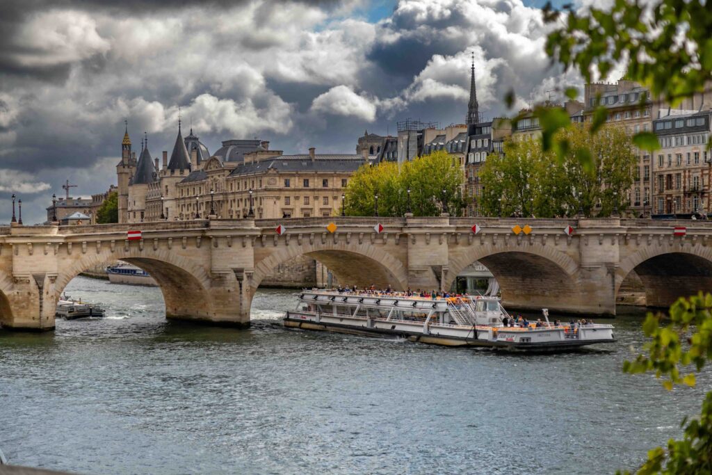 3 Days in Paris Itinerary (2026): The Ultimate Paris Vacation Guide A Seine river cruise boat passing under Pont Neuf bridge by the Conciergerie in Paris.