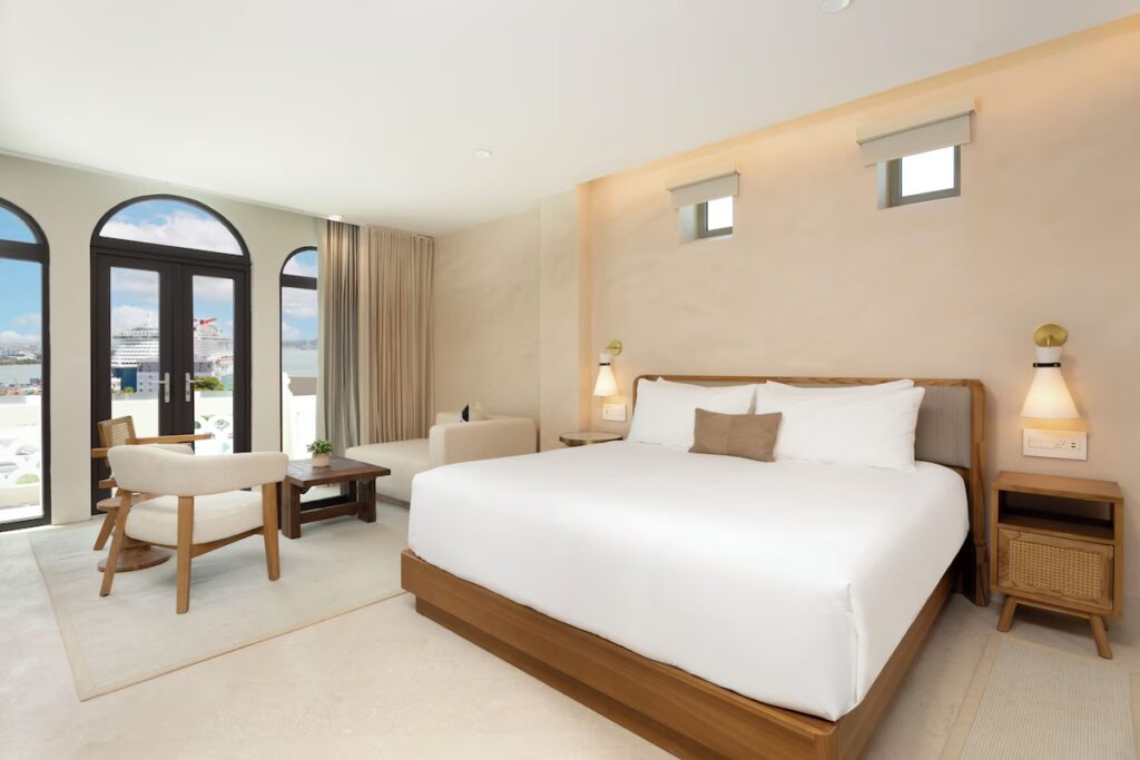 Minimalist, light-filled hotel room with wooden furniture and arch windows at Alma San Juan. 