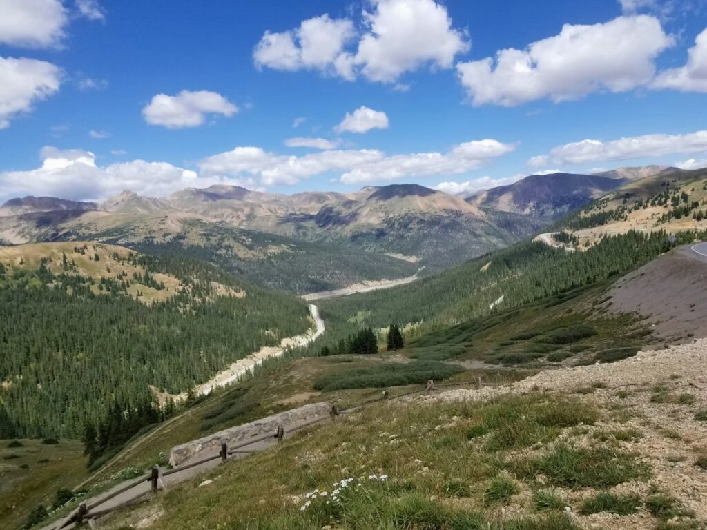 Best Time to Visit Colorado: A Month-by-Month Guide for Skiing, Hiking & Leaf-Peeping Winding mountain road in a green alpine valley under a bright blue sky.