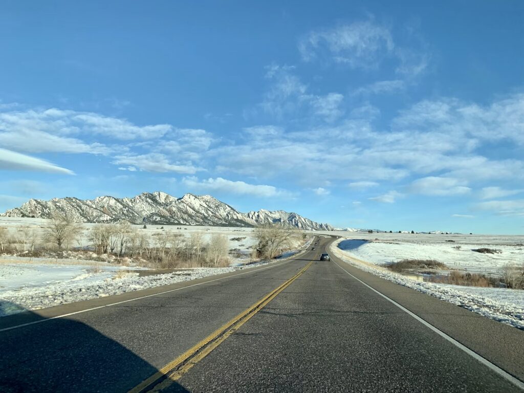 A paved road leading toward snow-dusted mountains under a blue sky. 
