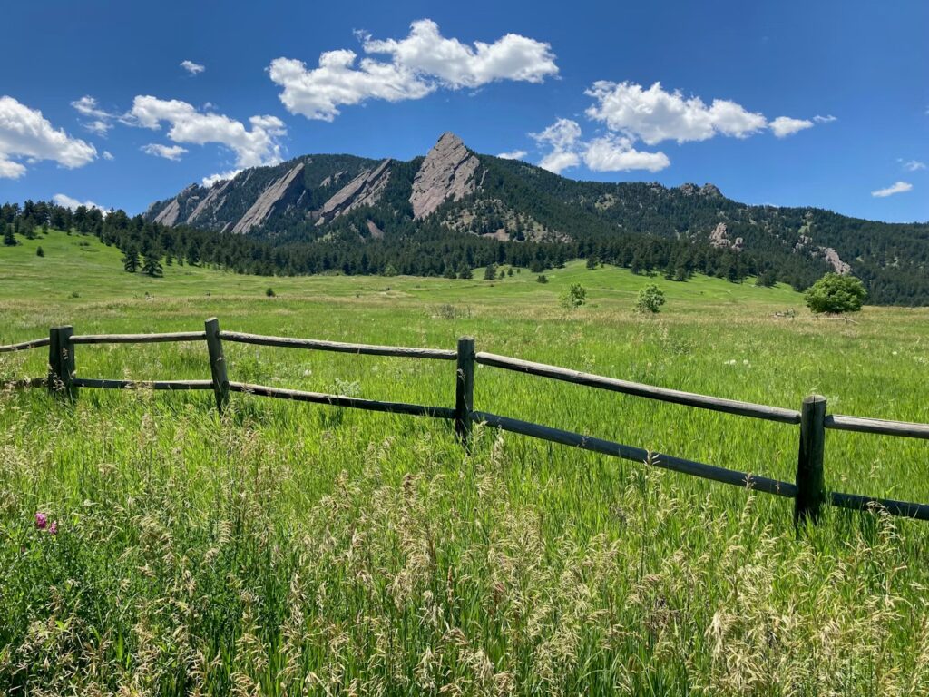The tilted sandstone Flatirons rising behind a green meadow in Boulder. 
