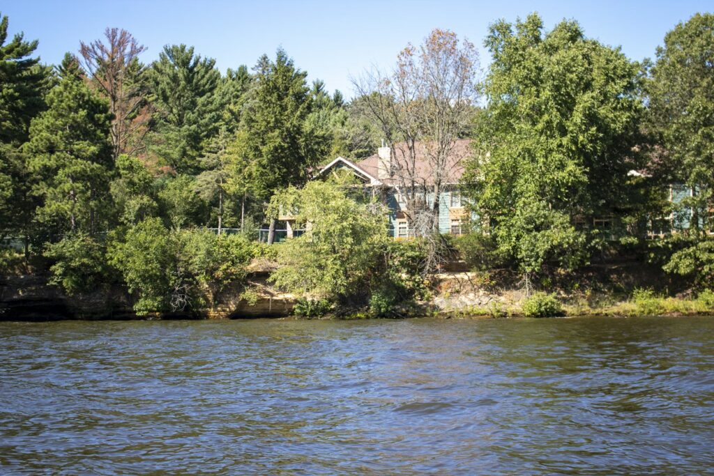 House surrounded by trees along a riverbank, viewed from across the water