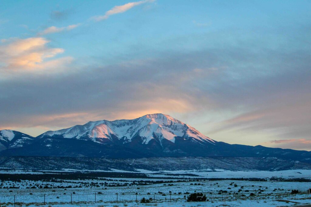 A snow-covered mountain glowing softly under a dawn or dusk sky 