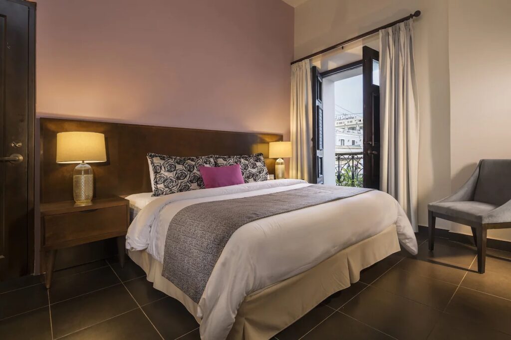 Cozy bedroom with wooden bed frame and doors opening to a juliet balcony at Decanter Hotel. 