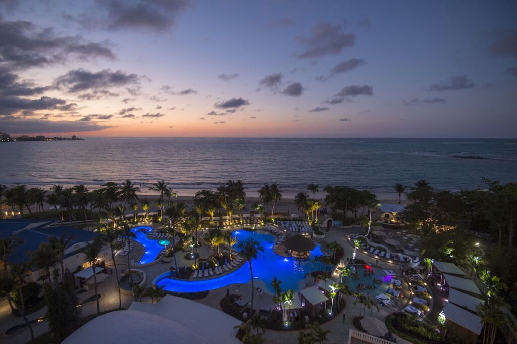 Large illuminated resort pool complex near the beach at dusk 