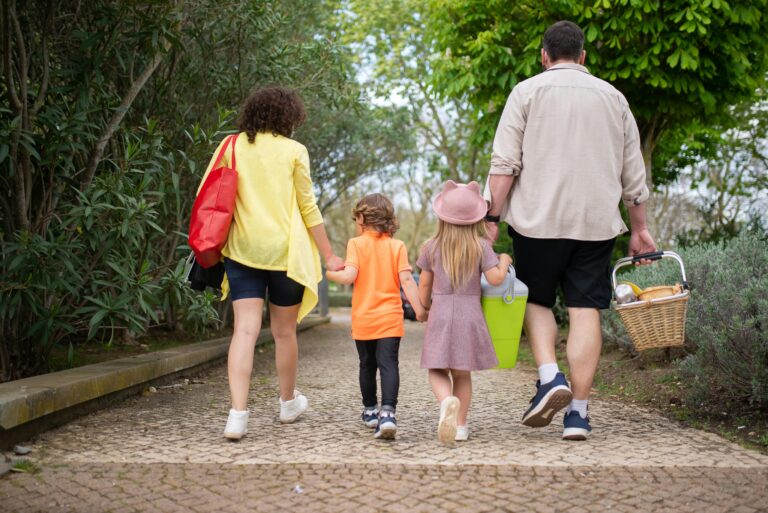 Family Travel Tips: 21 Genius Ways to Plan Fun Vacations for Kids A relaxed family of four walking down a sunny path with a picnic basket, enjoying fun vacations for kids thanks to smart family travel tips