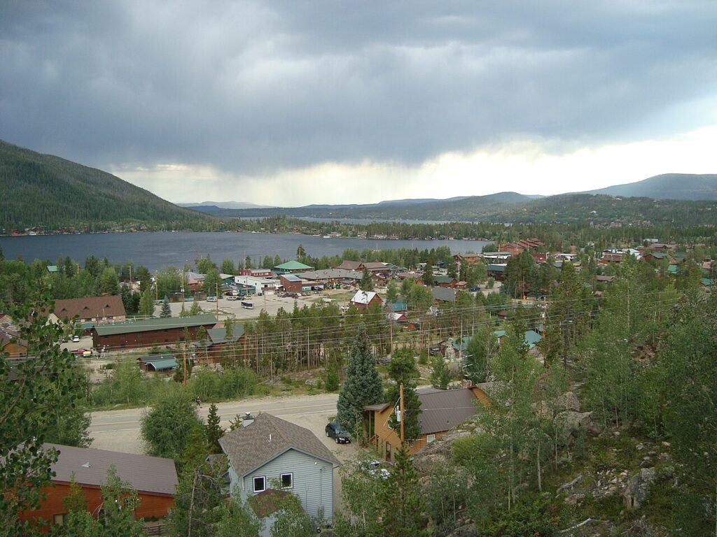 Grand Lake town and its calm water surrounded by green hills under a cloudy sky. 