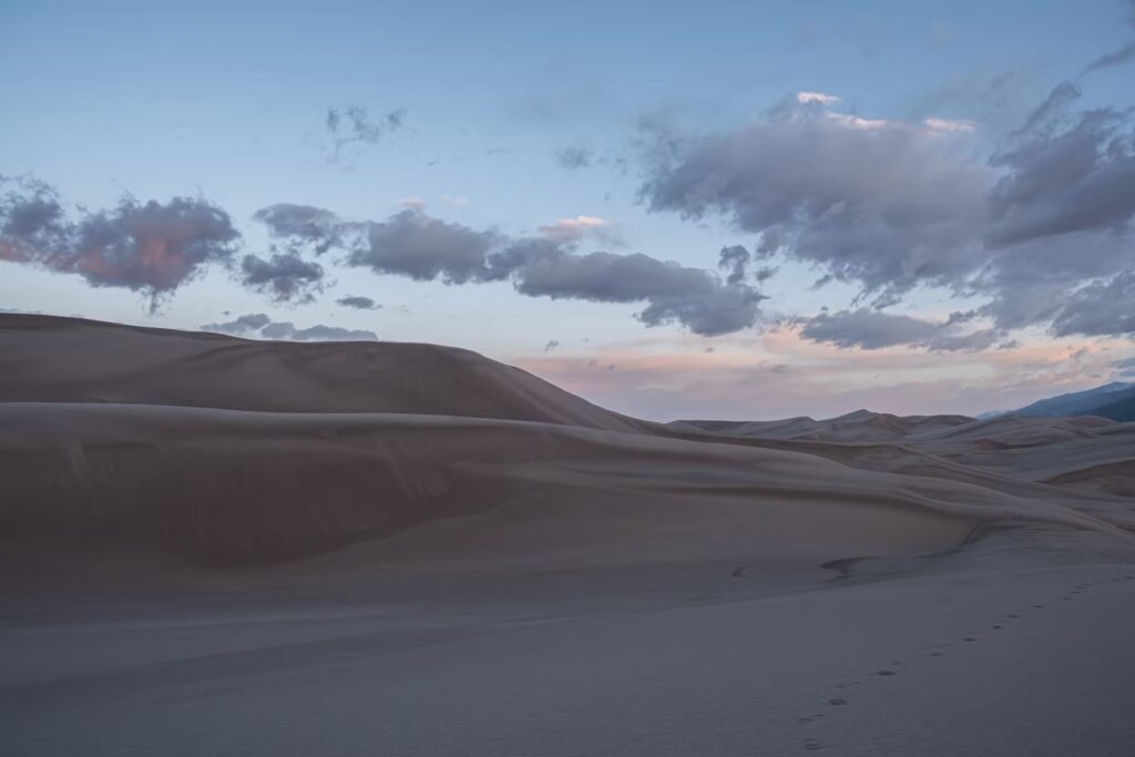Shadowy sand dunes under a purple and pink twilight sky. 
