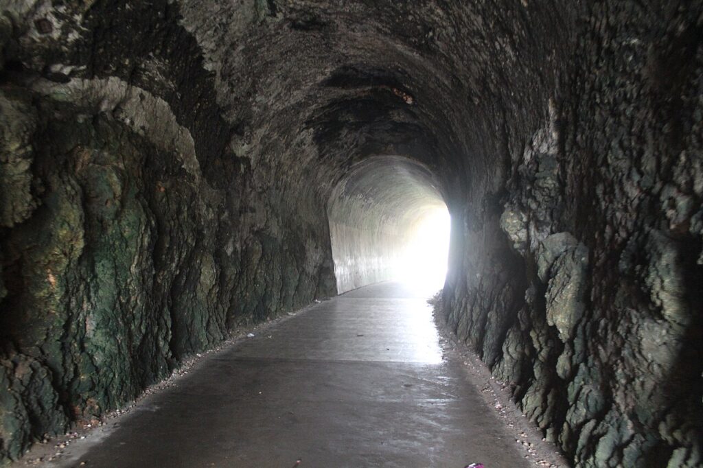 Dark Guajataca Tunnel carved through solid rock with light at the end. 
