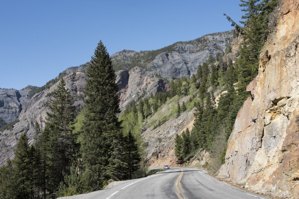 Winding highway cut into a steep rocky cliffside in the San Juan Mountains. 
