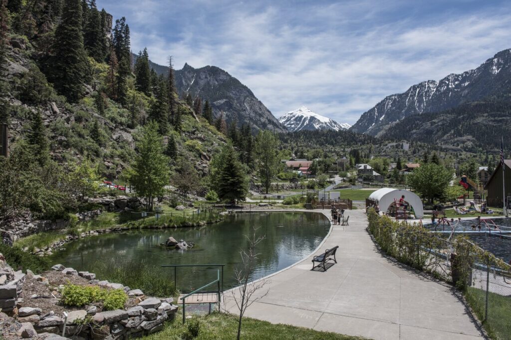 A peaceful hot spring surrounded by trees, rocks, and a playground in a valley. 