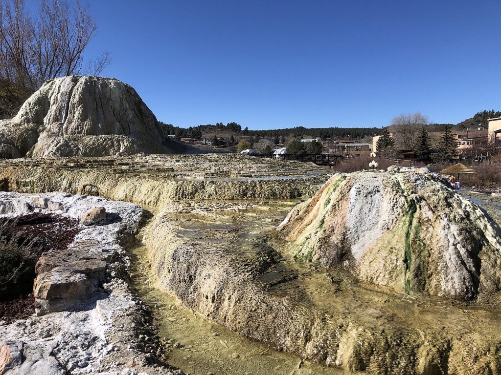 Natural mineral hot springs flowing over a rocky mound under a clear blue sky. 