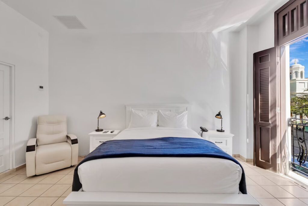 Basic bright hotel room with a white leather chair and balcony access at Hotel Plaza de Armas. 