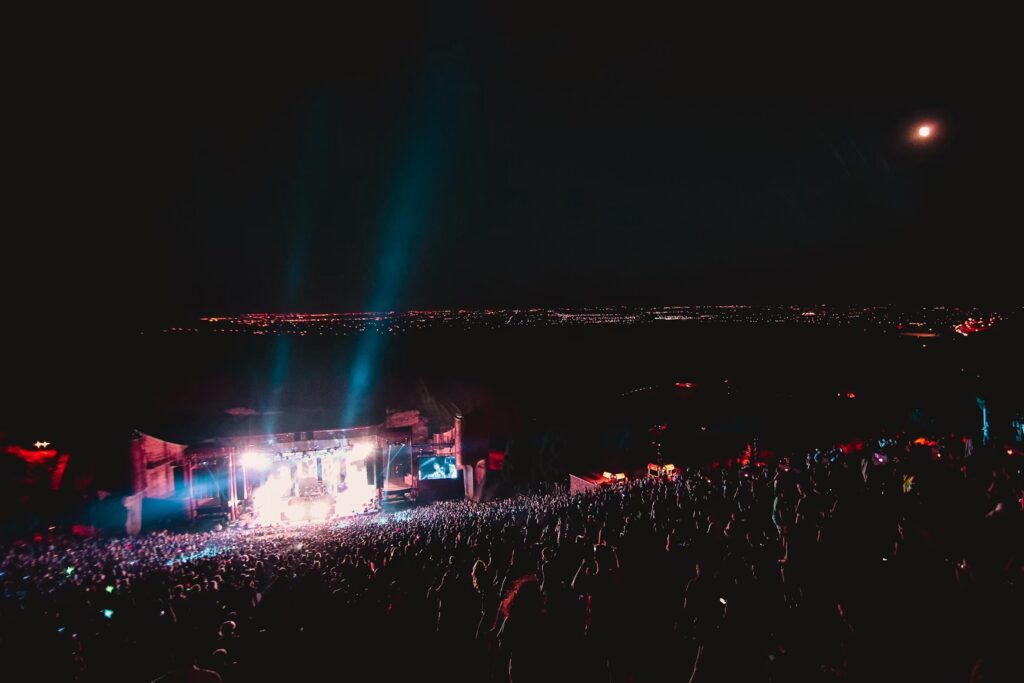 Bright stage lights illuminating a nighttime outdoor concert crowd. 