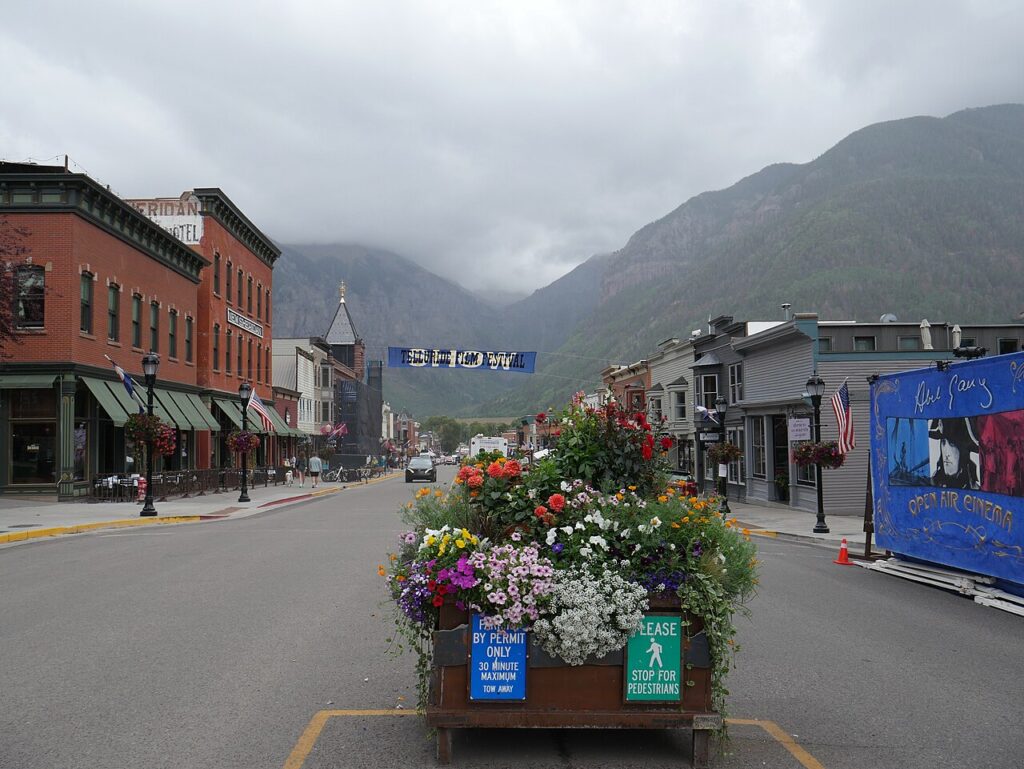 Historic main street in Telluride featuring a flower planter, brick buildings, and mountains in the background. 