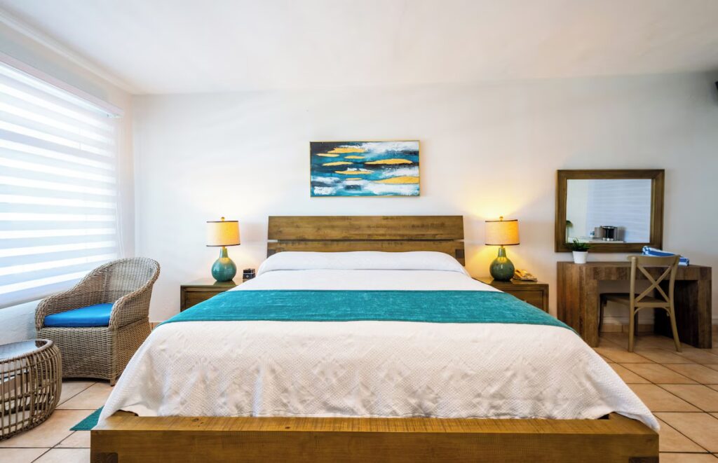 Cozy wooden bed in a bright, beach-style room with blue accents at Villa Cofresi Hotel. 