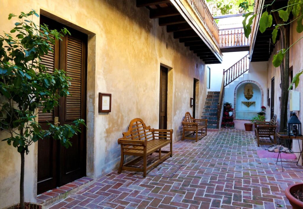 Narrow brick-paved interior courtyard walkway with wooden benches at Villa Herencia. 