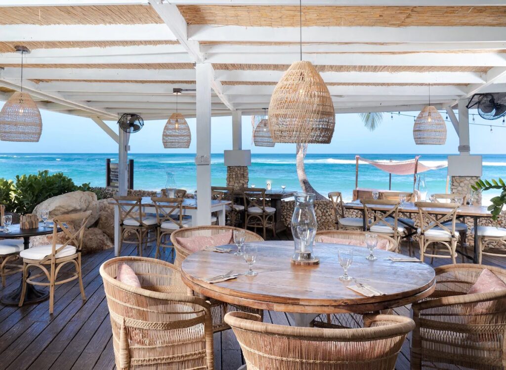 Open-air beachfront dining area with rustic tables and woven lamps 