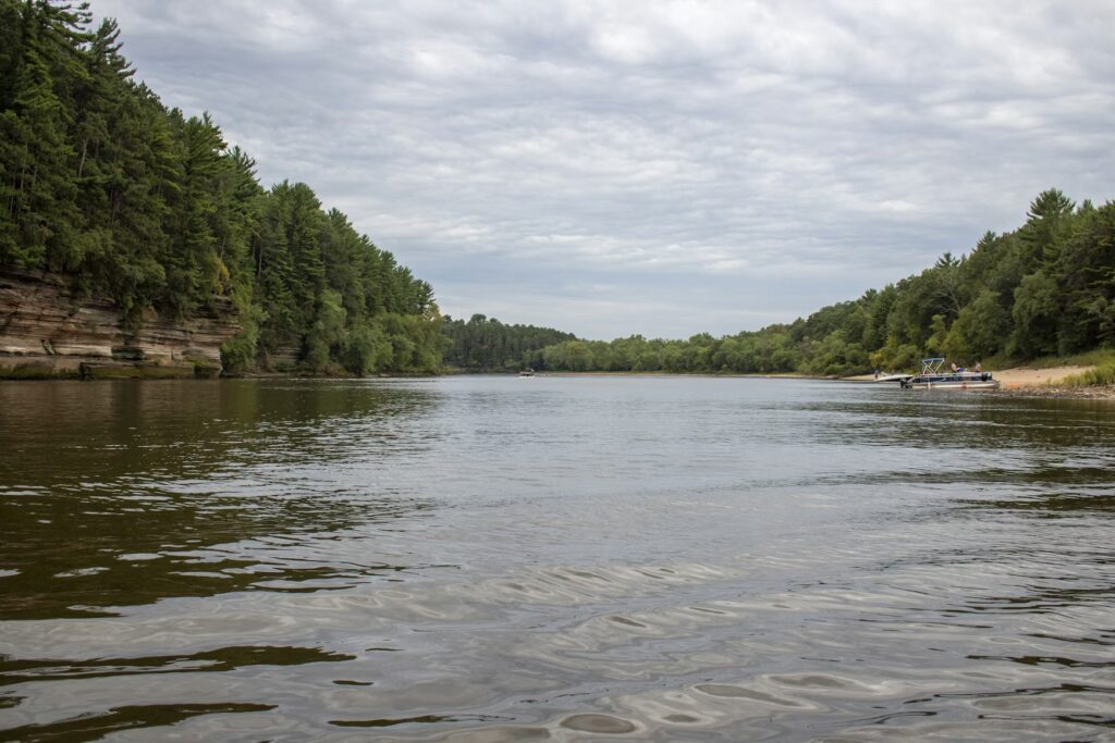 Calm river with forested banks and a small boat docked on a sandy shore