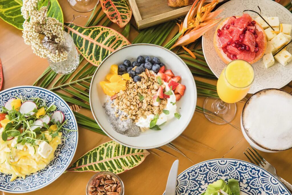 Healthy breakfast spread with yogurt bowls, fruits, and juices on tropical leaves 