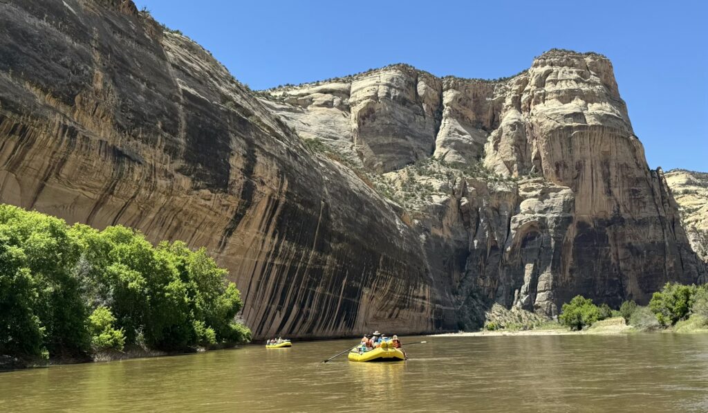 People in yellow rafts floating down a calm river surrounded by massive stone cliffs. 