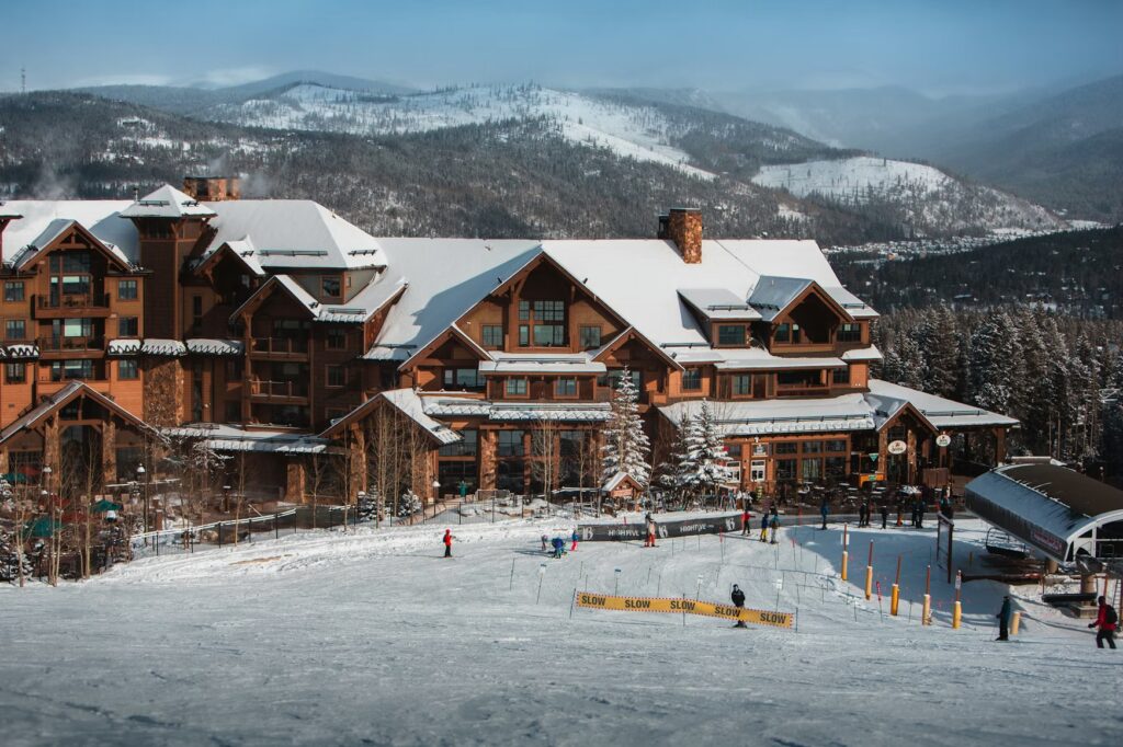 A large timber-framed ski resort lodge at the base of a snowy mountain. 