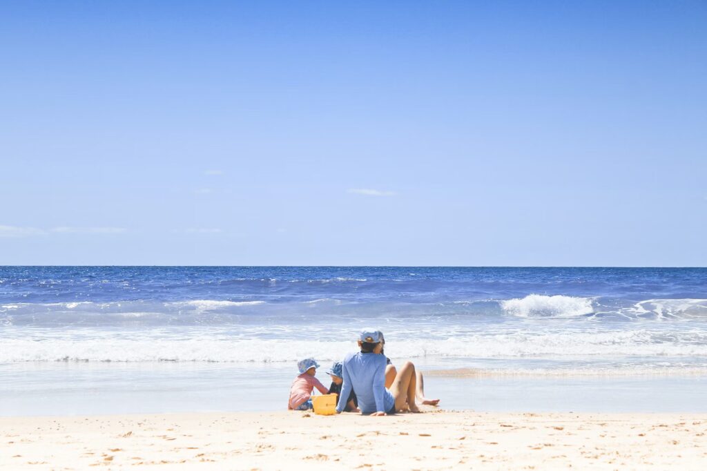 A parent relaxing on the beach while kids play safely in the sand, demonstrating a slow-paced approach for stress-free vacations