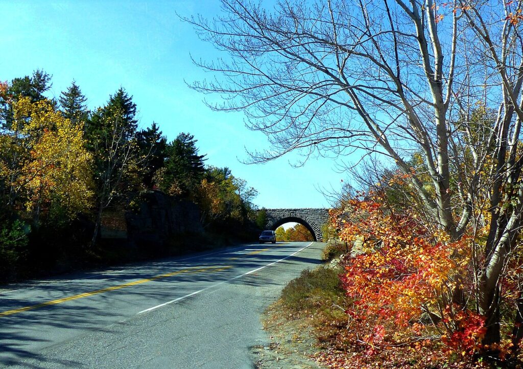 An arched stone bridge spanning a scenic paved road surrounded by autumn foliage in Acadia National Park.