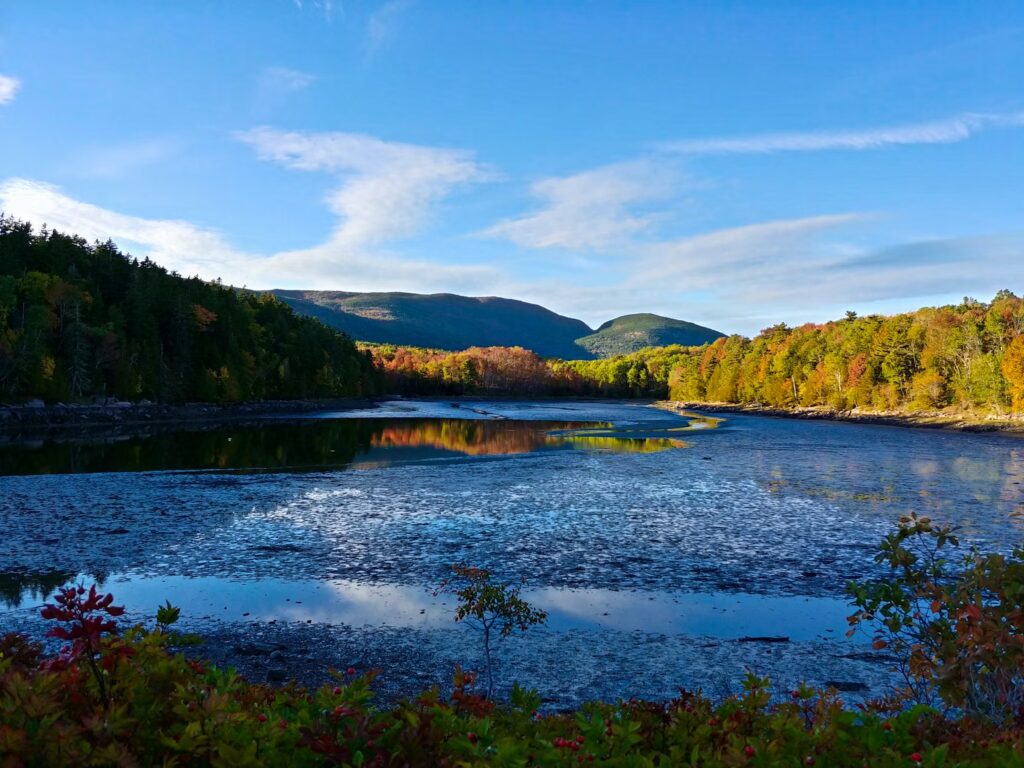 A calm lake reflecting nearby hills and colorful autumn forests in Acadia National Park, Maine.