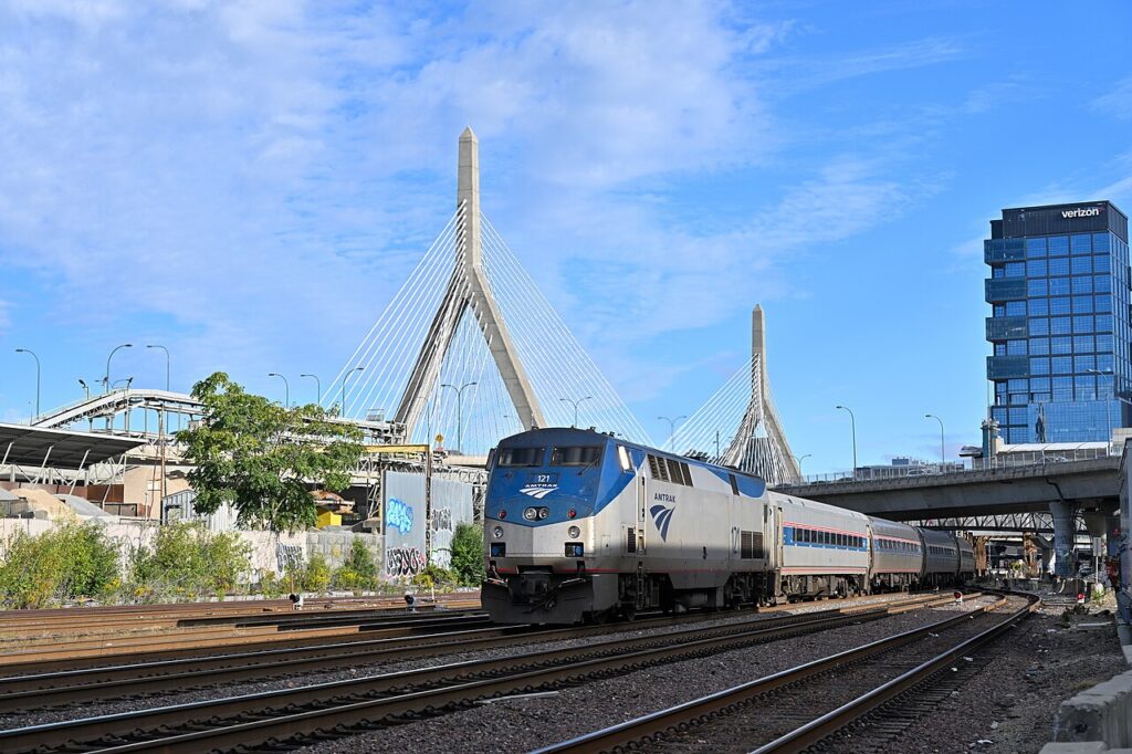 An Amtrak Downeaster train approaching Boston North Station with the iconic Zakim Bridge in the background.