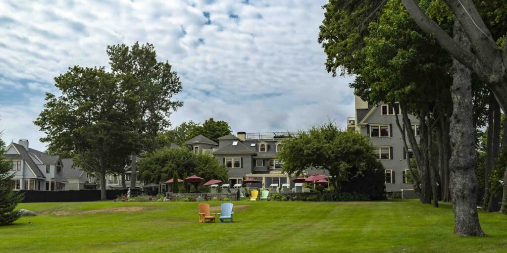 A lush green lawn with colorful Adirondack chairs sitting in front of a historic resort building.